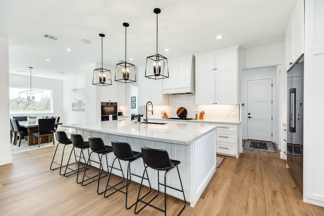 kitchen with tasteful backsplash, visible vents, light wood-type flooring, custom range hood, and a large island