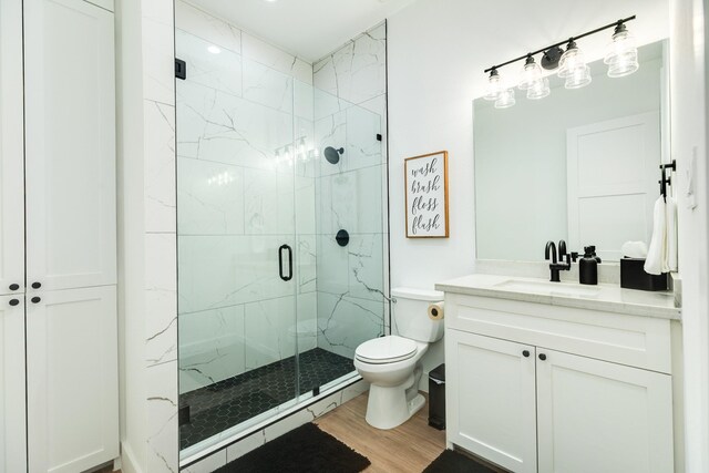 bathroom with a marble finish shower, toilet, wood finished floors, and vanity