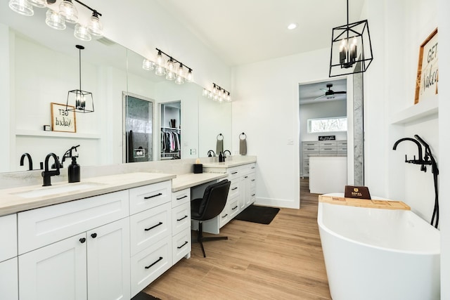 bathroom with a ceiling fan, wood finished floors, a freestanding tub, two vanities, and a sink