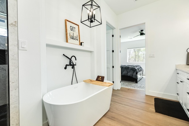 ensuite bathroom featuring vanity, wood finished floors, baseboards, a soaking tub, and ensuite bathroom