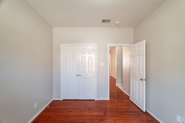 unfurnished bedroom with wood finished floors, visible vents, a closet, and baseboards