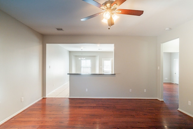 unfurnished room featuring visible vents, ceiling fan with notable chandelier, baseboards, and wood finished floors