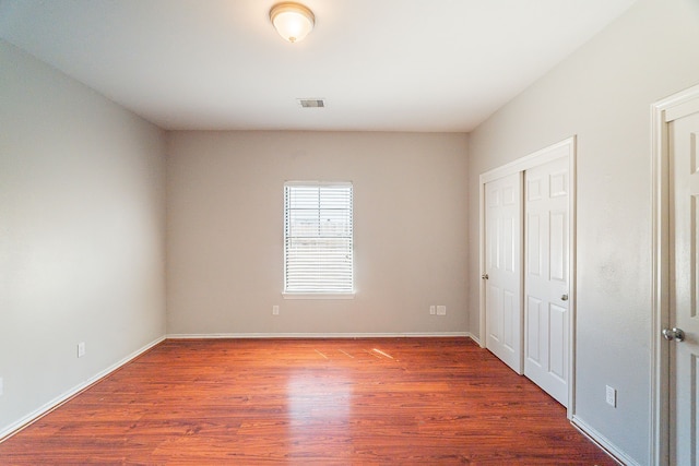 unfurnished bedroom featuring visible vents, baseboards, a closet, and wood finished floors