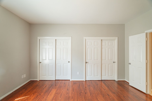 unfurnished bedroom with baseboards, multiple closets, and dark wood-style flooring