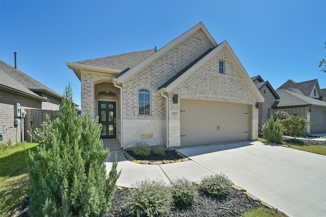 french country style house with brick siding, concrete driveway, a garage, and roof with shingles