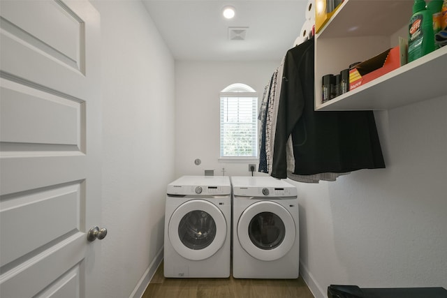 laundry room with wood finished floors, baseboards, visible vents, washing machine and clothes dryer, and laundry area