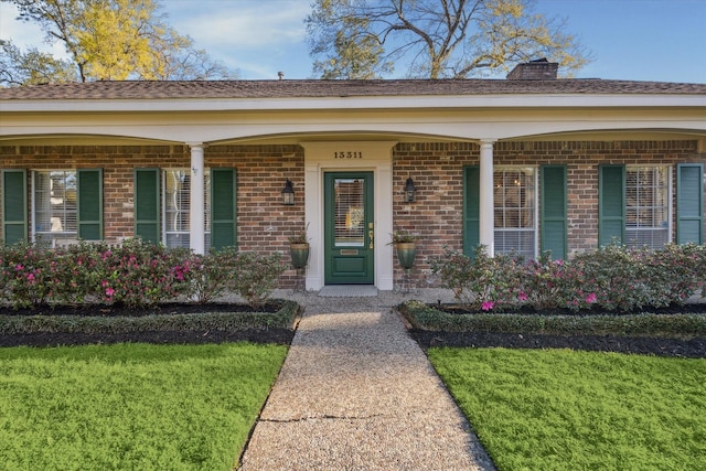 doorway to property with a chimney, brick siding, a porch, and a lawn