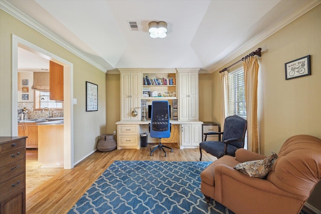 office area with visible vents, crown molding, lofted ceiling, built in desk, and light wood-style floors