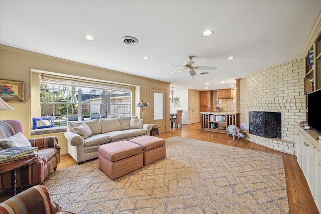 living room featuring visible vents, a brick fireplace, light wood-style flooring, and a ceiling fan