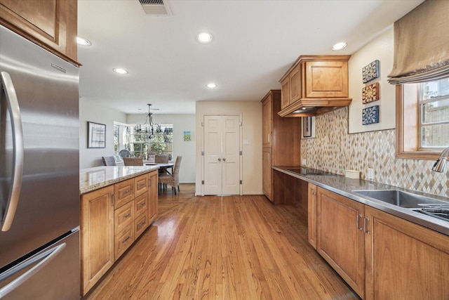 kitchen with visible vents, brown cabinets, stainless steel fridge, black electric stovetop, and light wood-type flooring