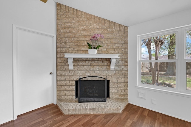 unfurnished living room with a brick fireplace, lofted ceiling, and wood finished floors