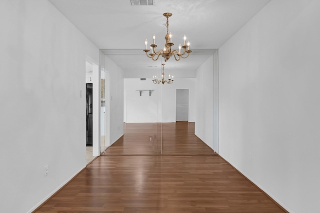 unfurnished dining area with visible vents, an inviting chandelier, and wood finished floors