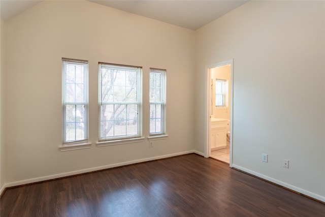 spare room featuring dark wood-type flooring, baseboards, and vaulted ceiling