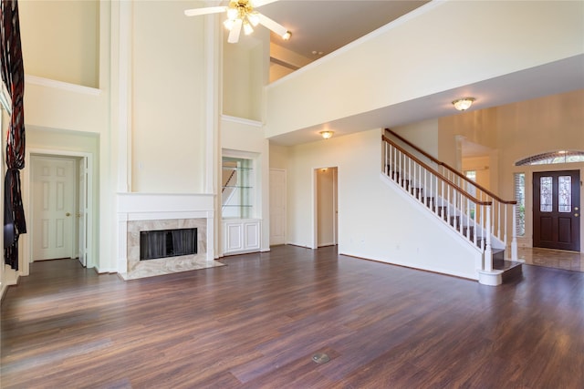 unfurnished living room featuring stairway, wood finished floors, baseboards, a high ceiling, and a fireplace