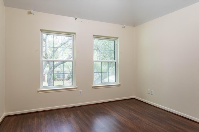 empty room featuring dark wood finished floors, baseboards, and a wealth of natural light