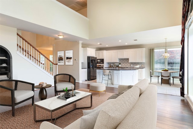 living room featuring stairs, light wood-style flooring, recessed lighting, and a high ceiling