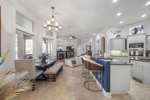 kitchen featuring dark countertops, ornamental molding, decorative backsplash, appliances with stainless steel finishes, and a glass covered fireplace