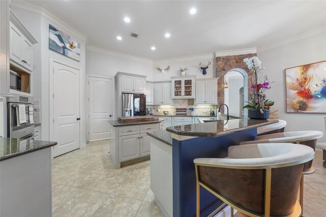 kitchen featuring a breakfast bar, arched walkways, a sink, stainless steel appliances, and a center island