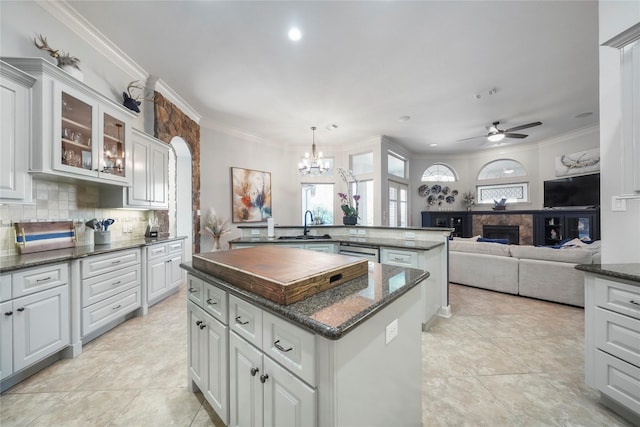 kitchen featuring a fireplace, glass insert cabinets, crown molding, backsplash, and a center island