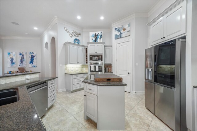 kitchen featuring stainless steel appliances, white cabinetry, crown molding, tasteful backsplash, and a center island