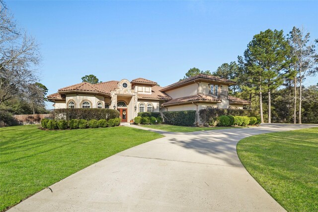 mediterranean / spanish-style home featuring a front lawn, a tiled roof, driveway, and stucco siding