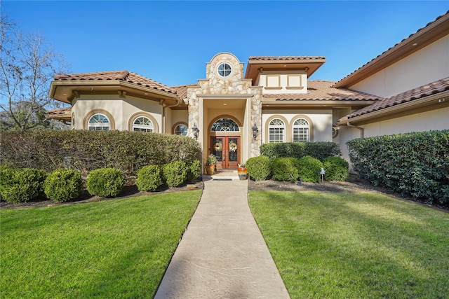 mediterranean / spanish house featuring a tile roof, a front yard, stucco siding, french doors, and stone siding