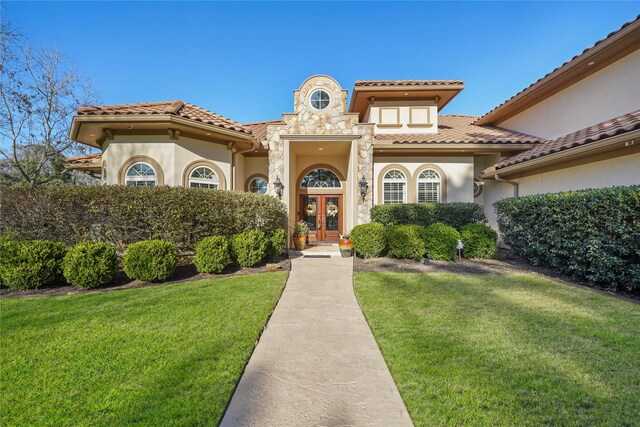 mediterranean / spanish house featuring a tile roof, a front yard, stucco siding, french doors, and stone siding