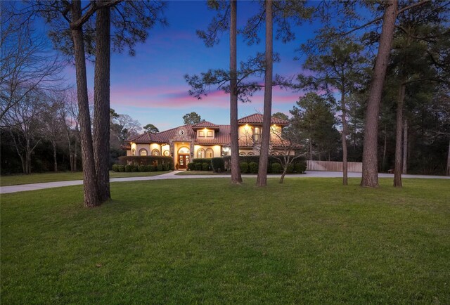 mediterranean / spanish home featuring a yard, curved driveway, and a tile roof