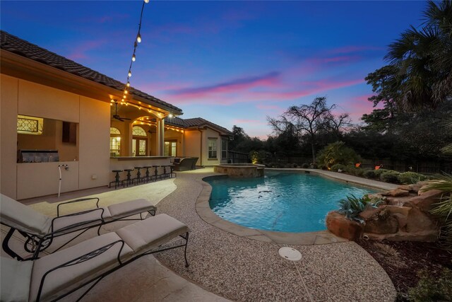 pool at dusk featuring a patio, outdoor dry bar, and a pool with connected hot tub