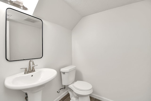 half bath featuring tile patterned flooring, baseboards, toilet, lofted ceiling, and a sink