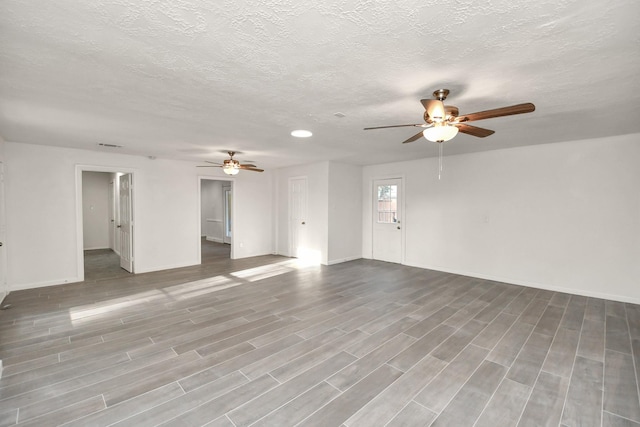 unfurnished living room with ceiling fan, baseboards, a textured ceiling, and wood finished floors