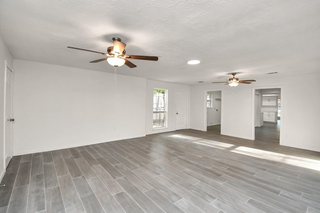 unfurnished living room featuring a ceiling fan, baseboards, a textured ceiling, and wood tiled floor