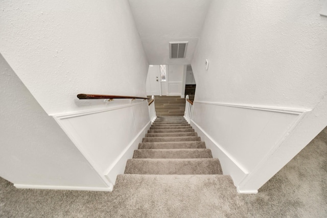 stairs featuring visible vents, wood finished floors, carpet flooring, and a textured wall