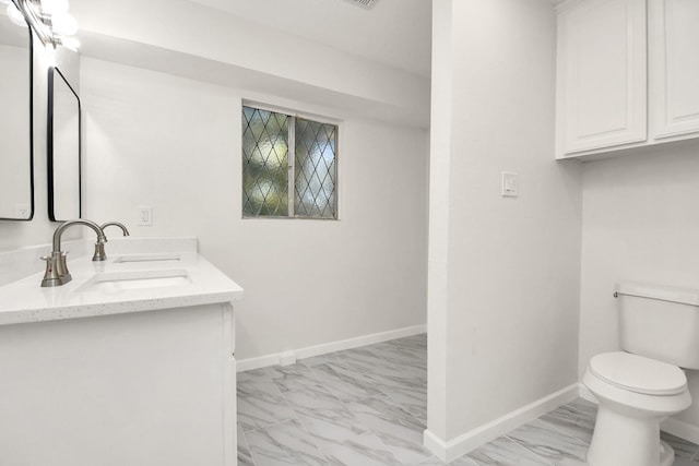 bathroom with marble finish floor, toilet, baseboards, and a sink