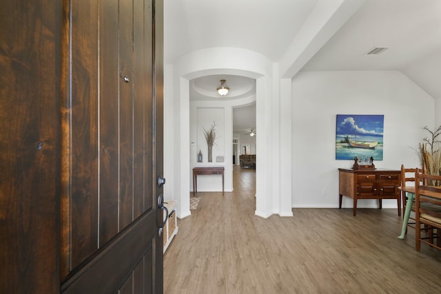 foyer with visible vents, arched walkways, lofted ceiling, and light wood-style flooring