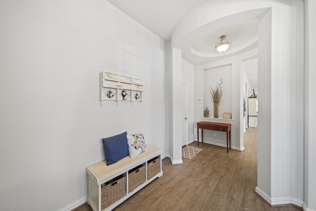 corridor with wood finished floors, baseboards, and arched walkways