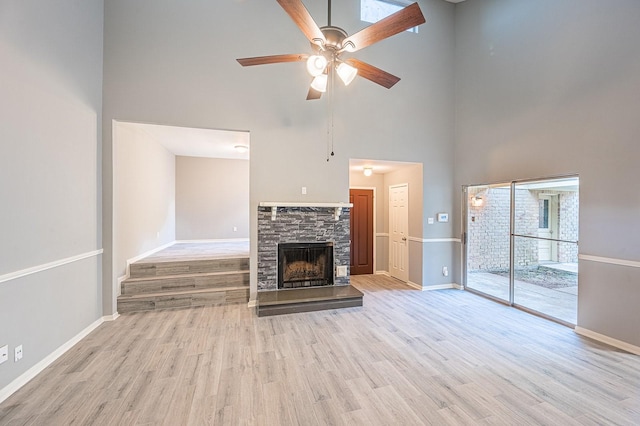 unfurnished living room with a stone fireplace, ceiling fan, baseboards, and wood finished floors