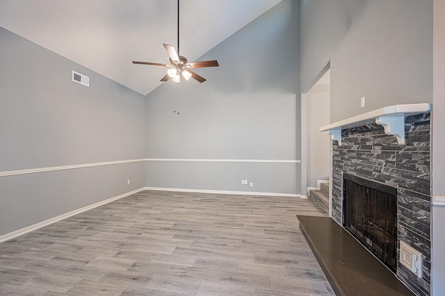 unfurnished living room with baseboards, a stone fireplace, wood finished floors, and a ceiling fan