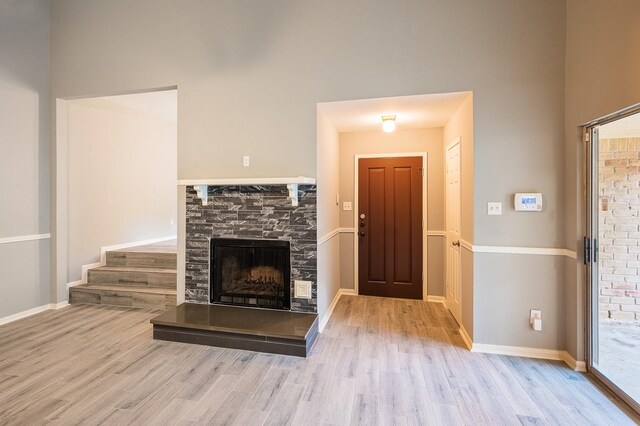 unfurnished living room with a fireplace with raised hearth, a high ceiling, baseboards, and wood finished floors