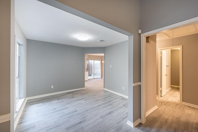 unfurnished room featuring light wood-style flooring, attic access, and baseboards