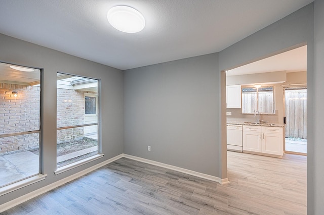 unfurnished dining area with a sink, baseboards, and light wood finished floors