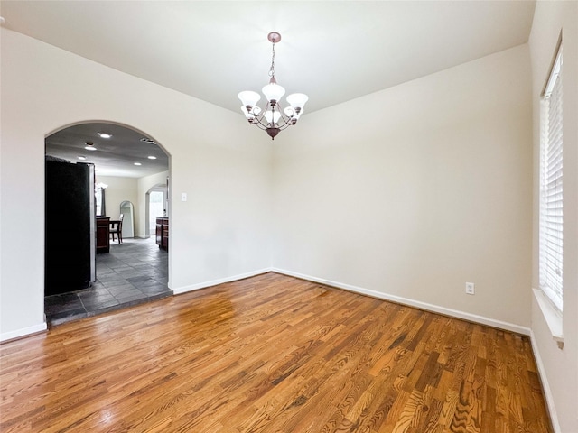 empty room with arched walkways, a chandelier, baseboards, and wood finished floors