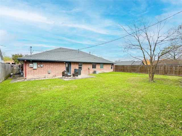 rear view of house featuring a patio, a fenced backyard, a yard, roof with shingles, and brick siding