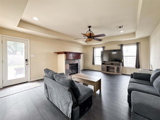 living area with visible vents, a tile fireplace, a tray ceiling, and wood finished floors