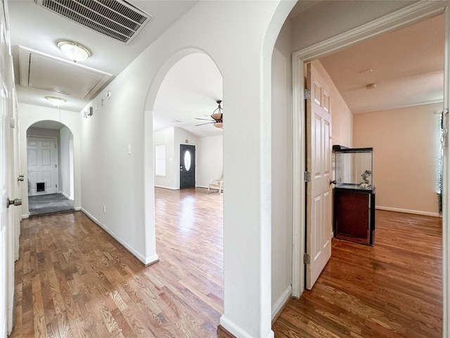 corridor with visible vents, wood finished floors, arched walkways, baseboards, and attic access