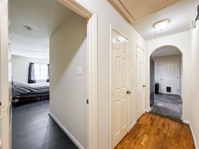 hallway featuring visible vents, wood finished floors, arched walkways, baseboards, and attic access