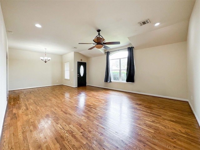 empty room with visible vents, ceiling fan with notable chandelier, wood finished floors, baseboards, and lofted ceiling