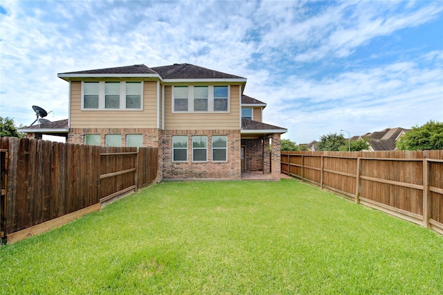 back of property featuring a yard, brick siding, a fenced backyard, and a shingled roof