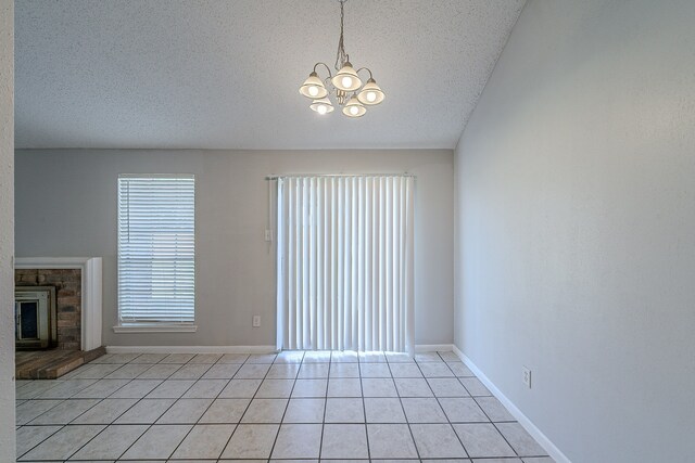 unfurnished living room with a textured ceiling, light tile patterned flooring, baseboards, a brick fireplace, and a chandelier