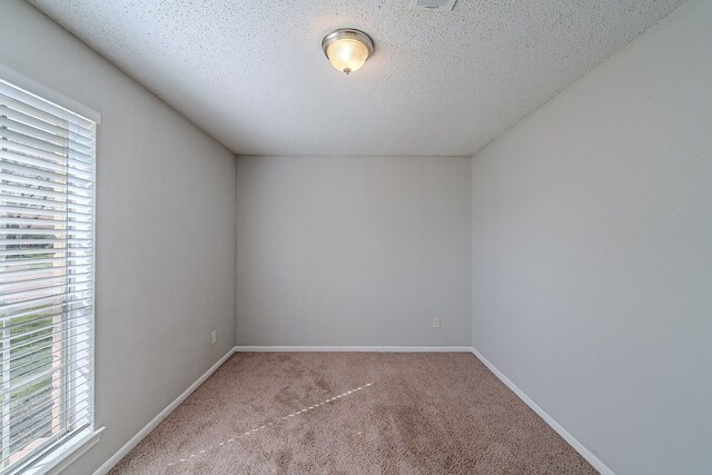 empty room with carpet, baseboards, and a textured ceiling